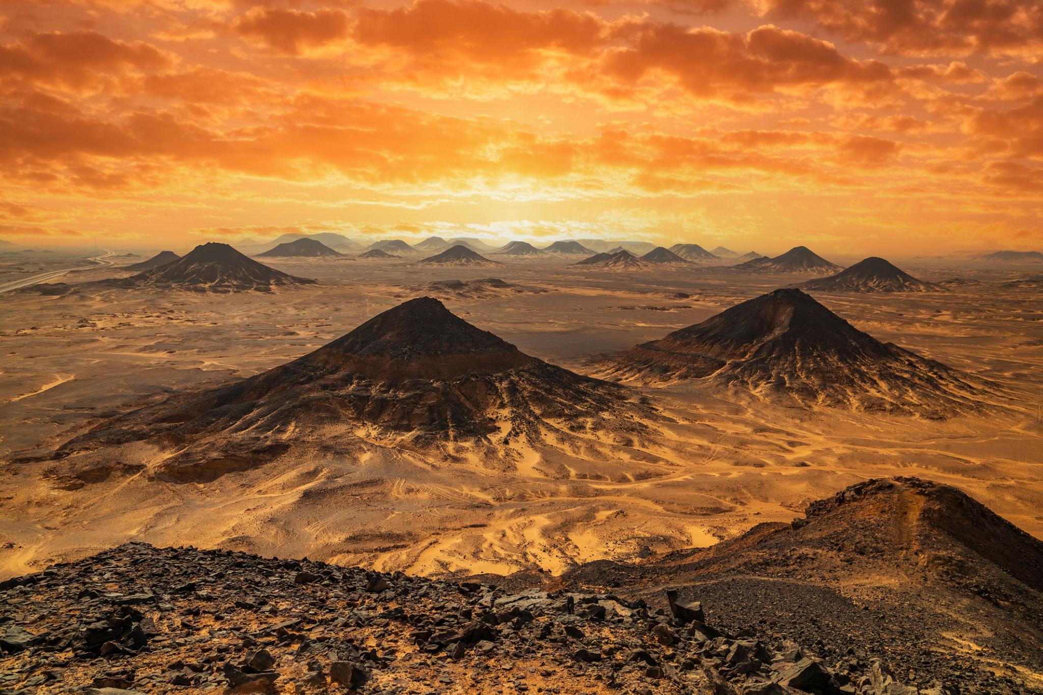 Panoramic view of dark volcanic cones rising from the Black Desert under a fiery orange sunset sky