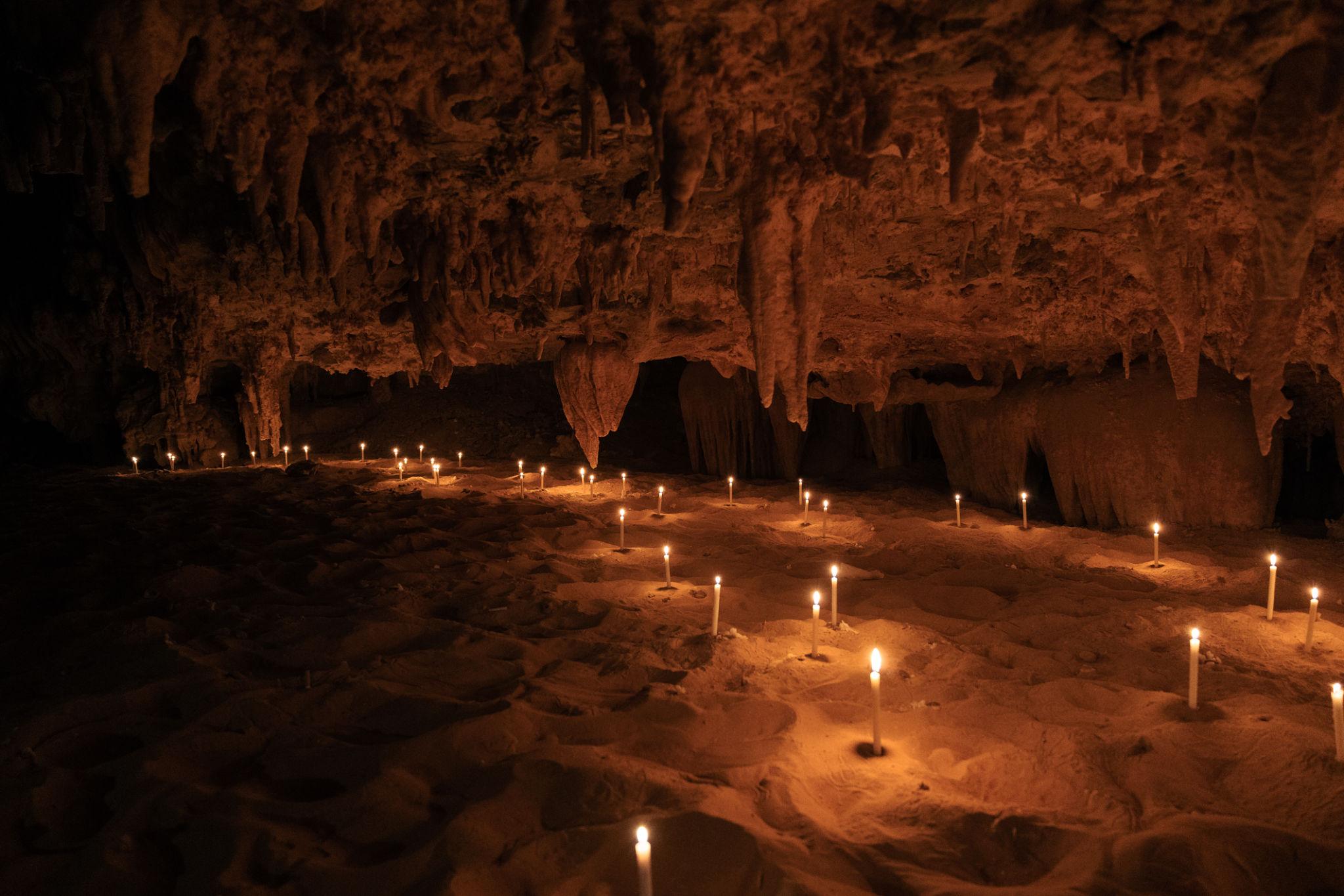 Dozens of candles illuminating a limestone cave floor with stalactites hanging from the ceiling