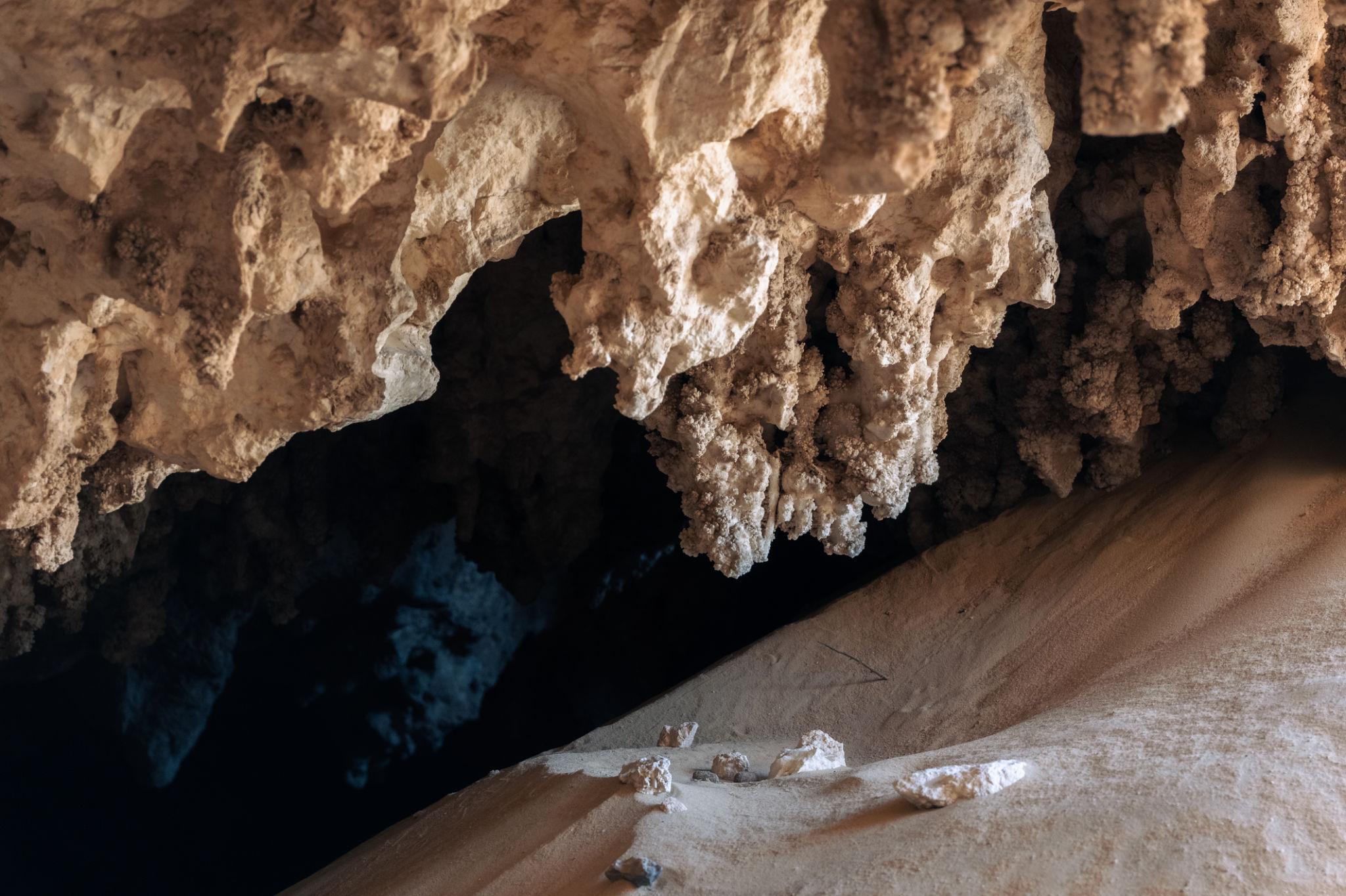 Crystal formations hanging inside a Bahariya Oasis cave with sandy floor below