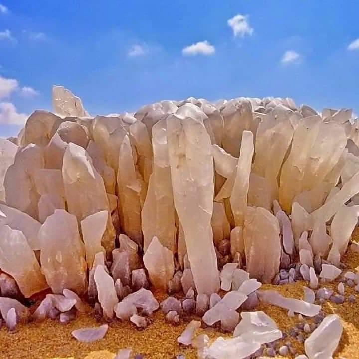 Large white quartz crystal cluster rising from golden desert sand under a blue sky