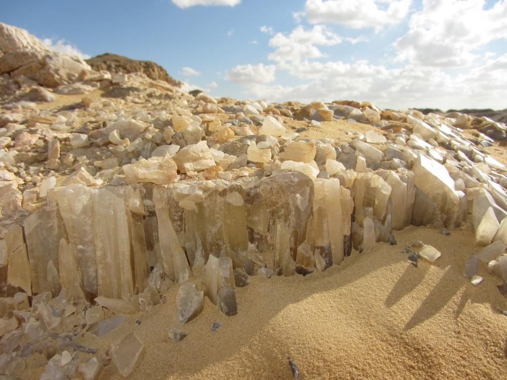 Close-up of translucent crystal formations jutting from sandy desert ground under a blue sky