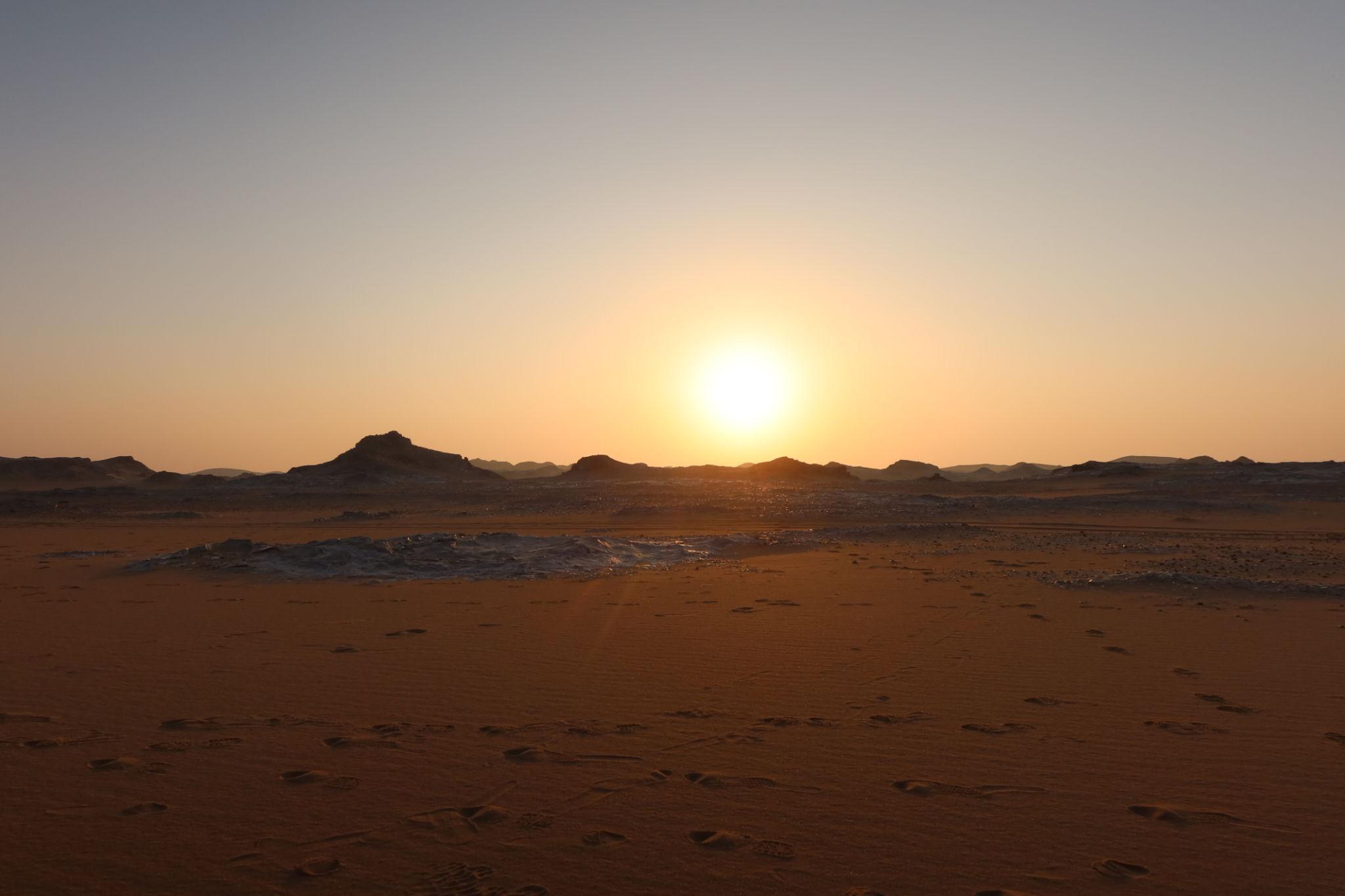 Golden sunset over rocky desert landscape with red sand and scattered white chalk formations