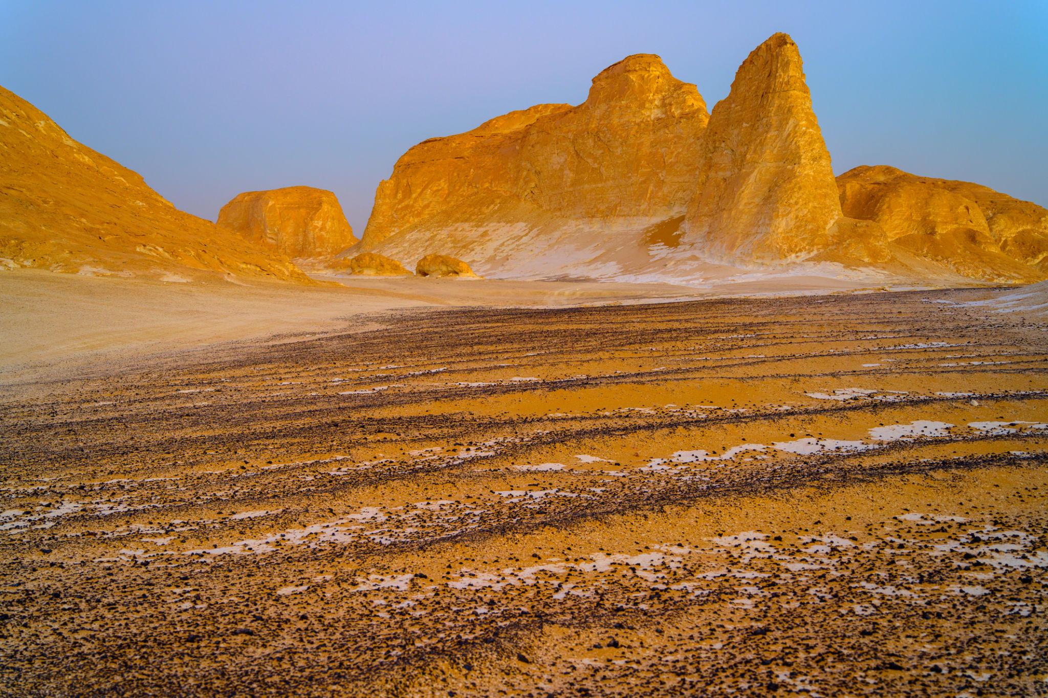 Towering golden limestone rock formations rise above a pebbled desert floor at dusk.