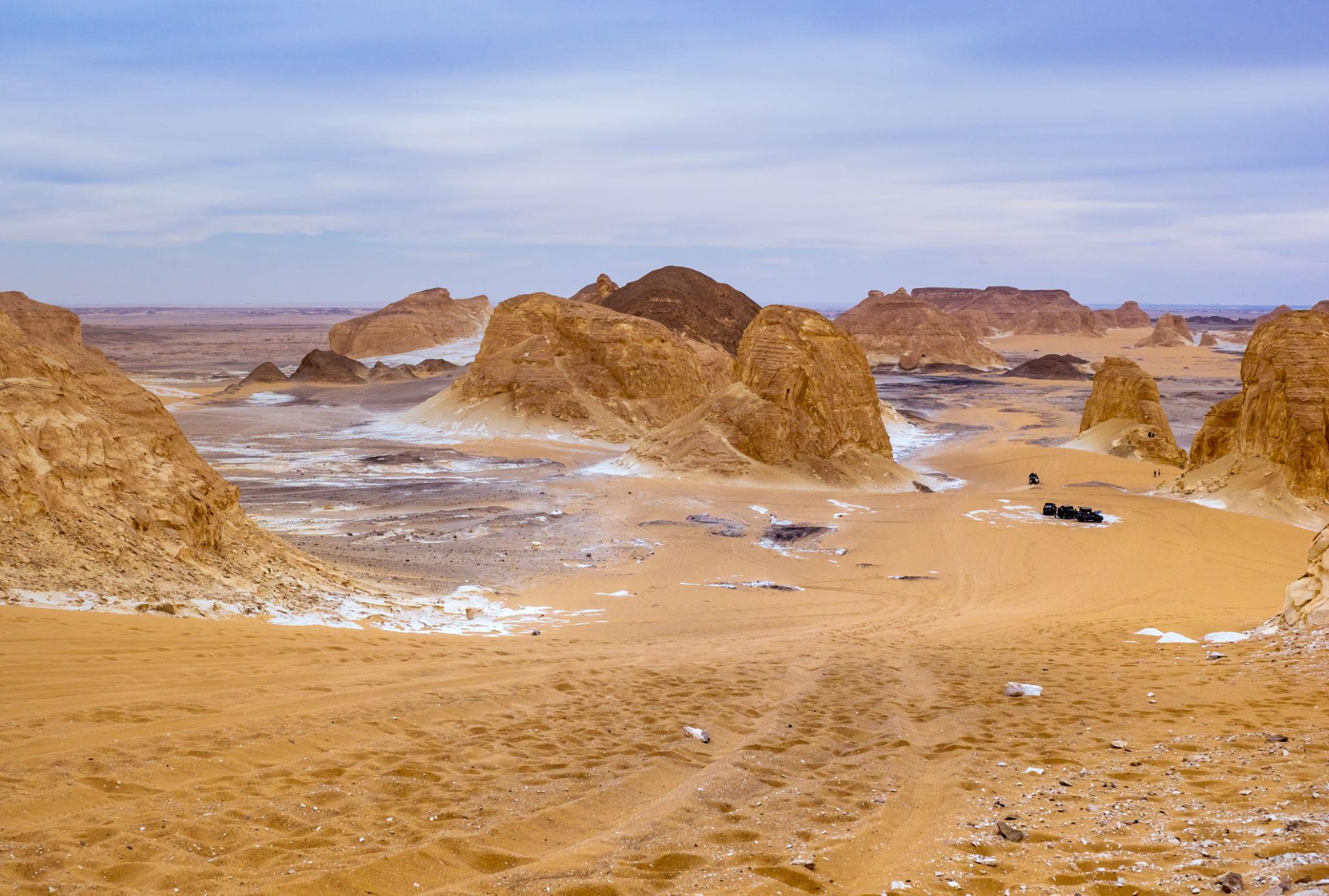 Golden sand dunes and eroded limestone rock formations stretch across the Bahariya desert landscape.