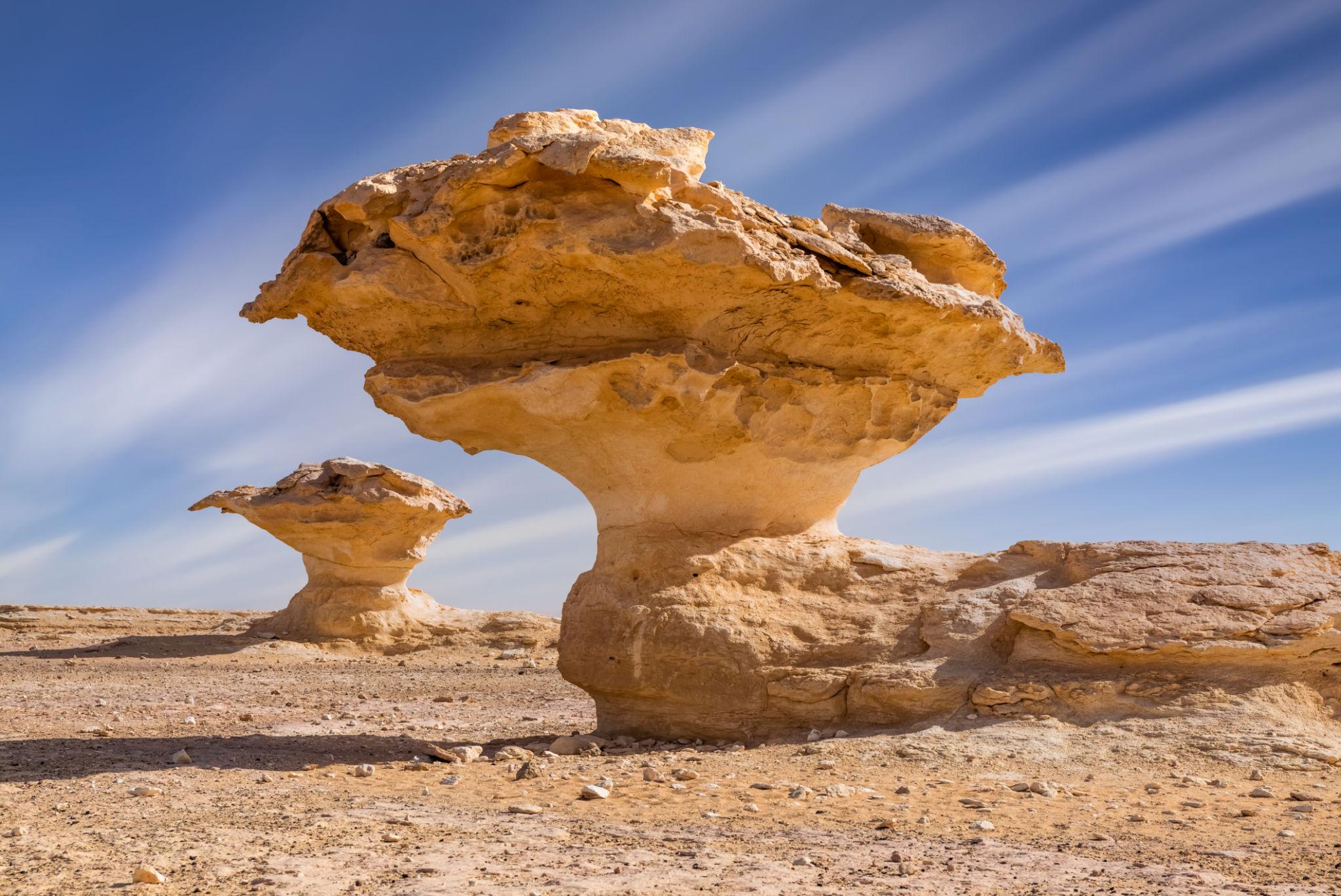 Two wind-eroded mushroom-shaped sandstone rock formations rising from the desert floor under a blue sky