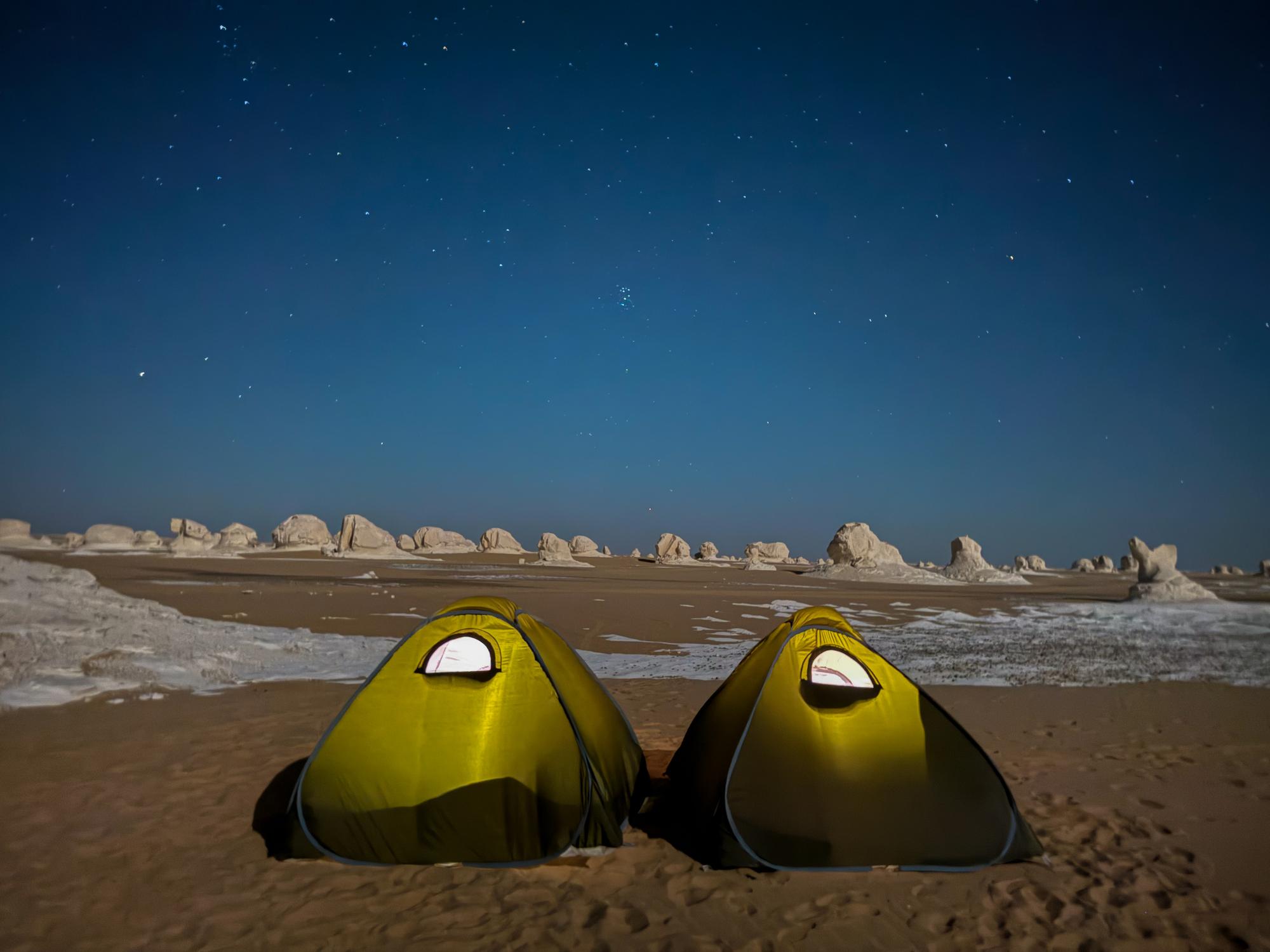 Two glowing yellow tents in Egypt's White Desert under a star-filled night sky