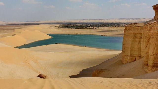 Turquoise lake nestled among sweeping golden sand dunes and sandstone cliffs in Fayoum