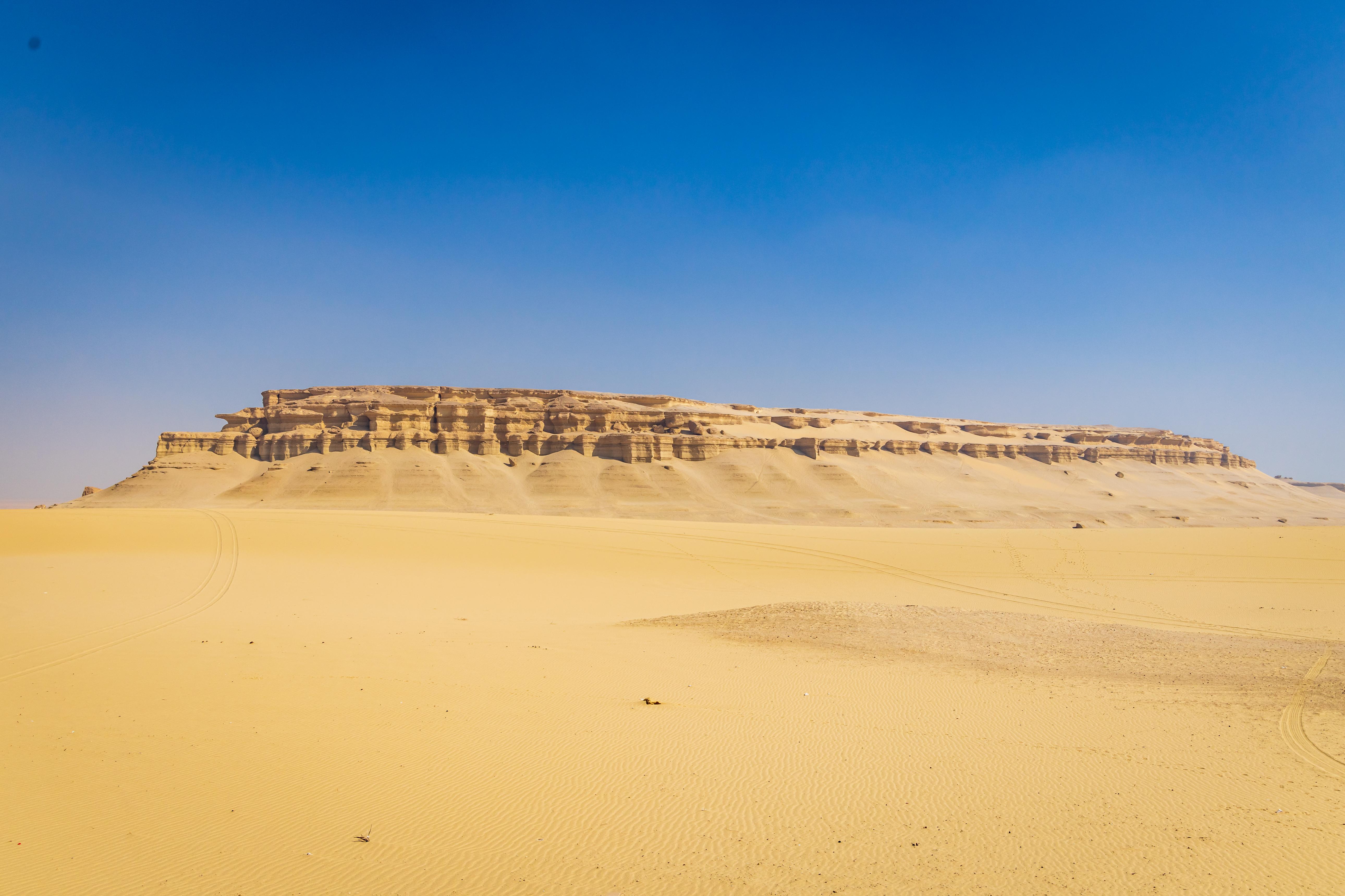 A flat-topped sandstone mesa rising above golden sand dunes under a clear blue sky