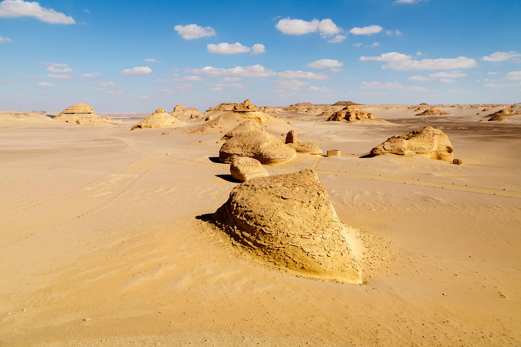 Eroded limestone rock formations rising from golden sand flats under a blue sky in Fayoum