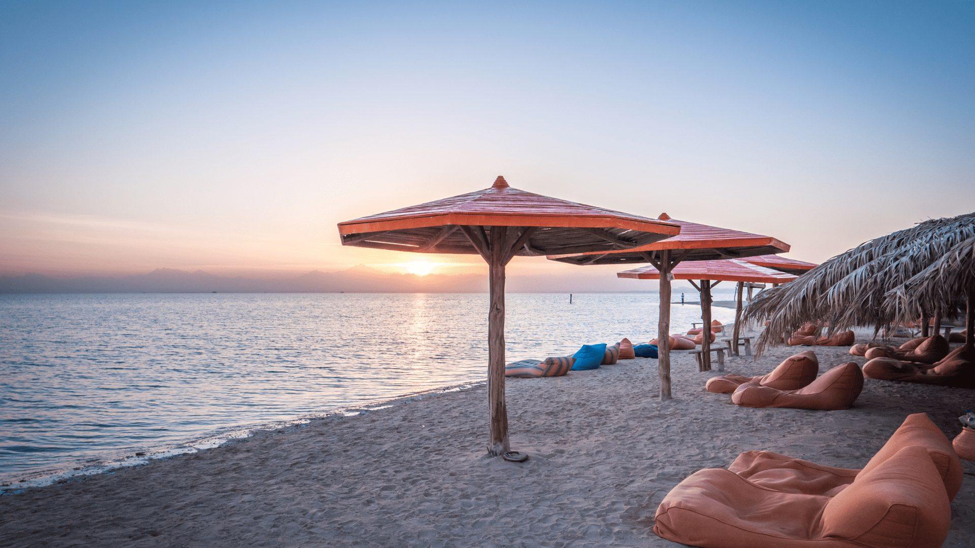 Wooden beach umbrellas and bean bags on a sandy Red Sea shore at sunset