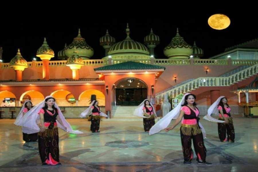 Belly dancers in colorful costumes perform at night outside an ornate domed resort building.
