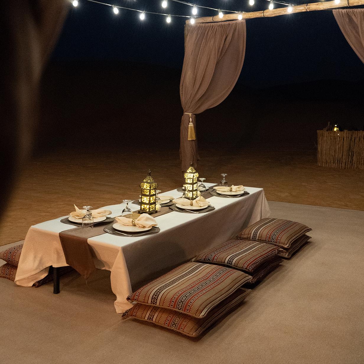 A low table set for four with Moroccan lanterns and floor cushions under string lights in the desert at night