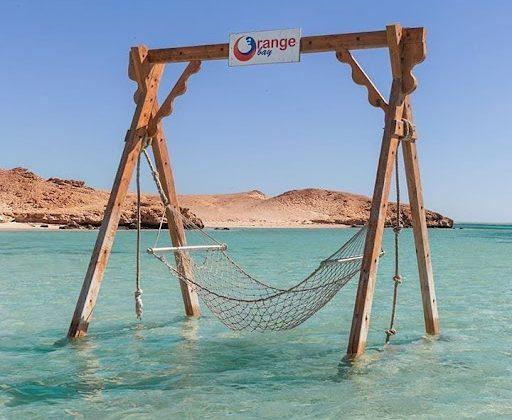 A rope hammock swing on a wooden frame standing in shallow turquoise Red Sea water