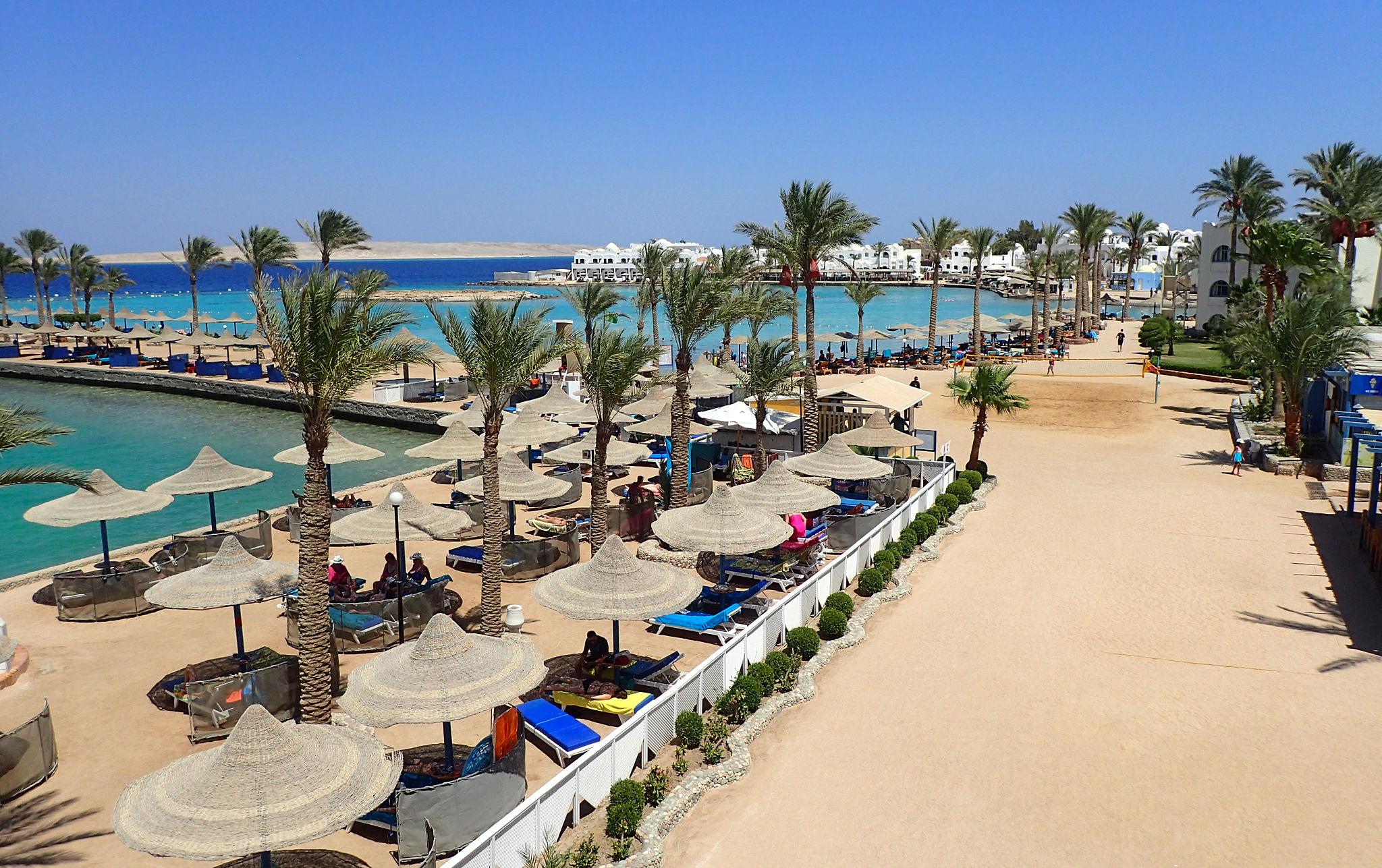 Hurghada beach resort with straw parasols, palm trees and turquoise Red Sea lagoon