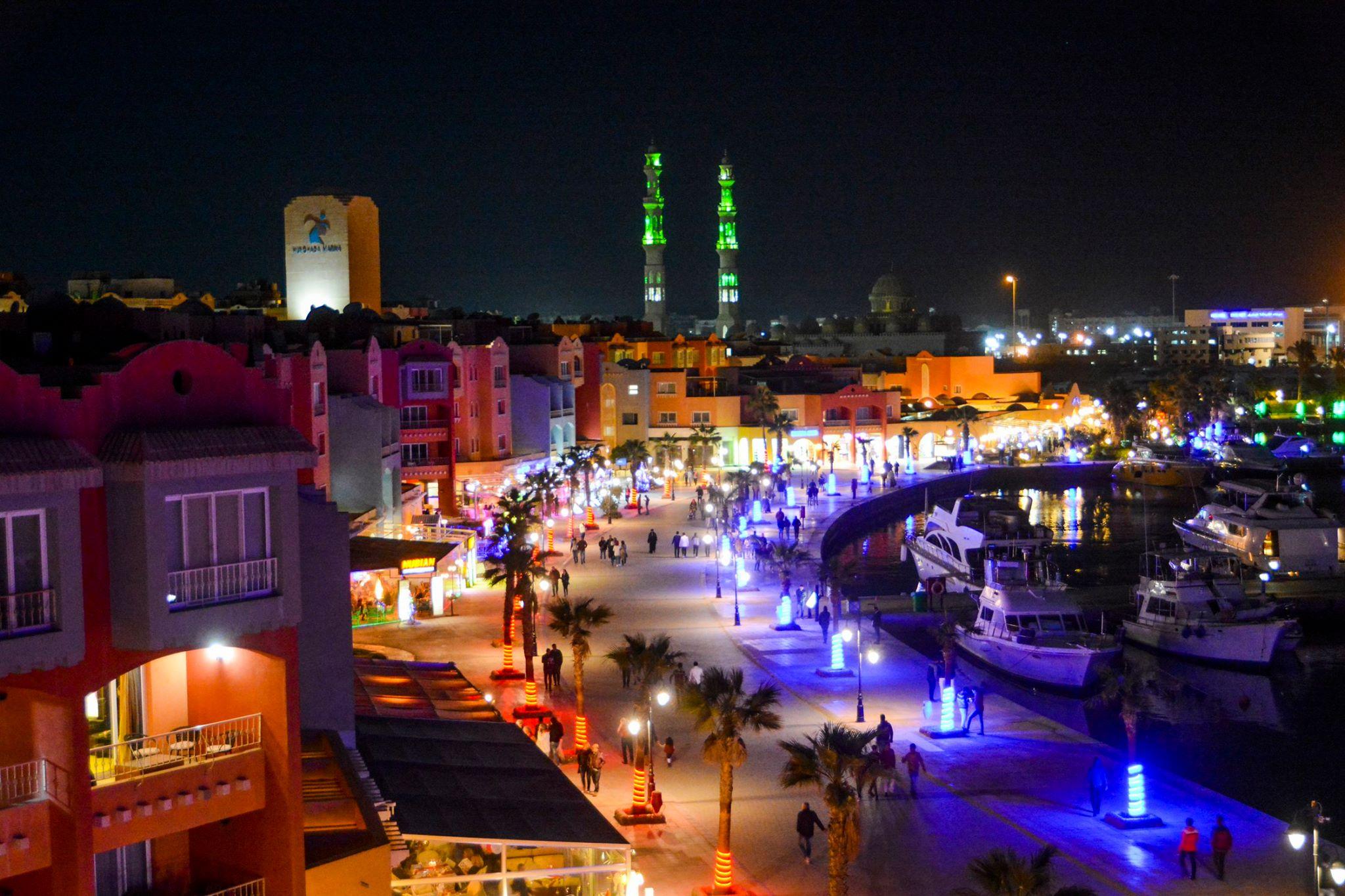 Hurghada marina promenade lit up at night with mosque minarets glowing green in the background