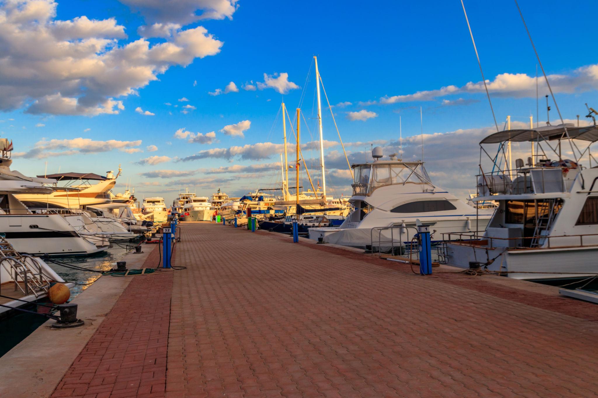 Luxury yachts moored along a brick promenade at a Red Sea marina under a blue sky
