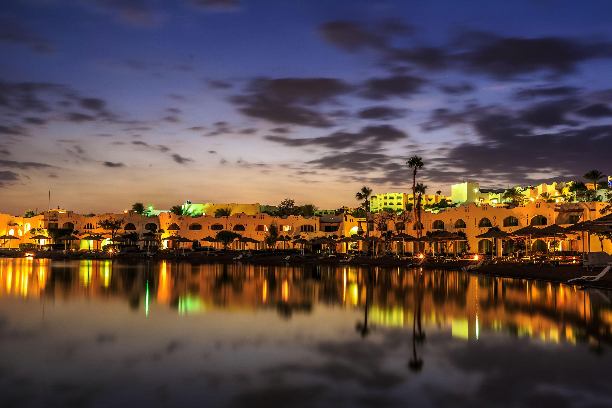 Illuminated Red Sea resort buildings reflecting golden light on a calm lagoon at dusk