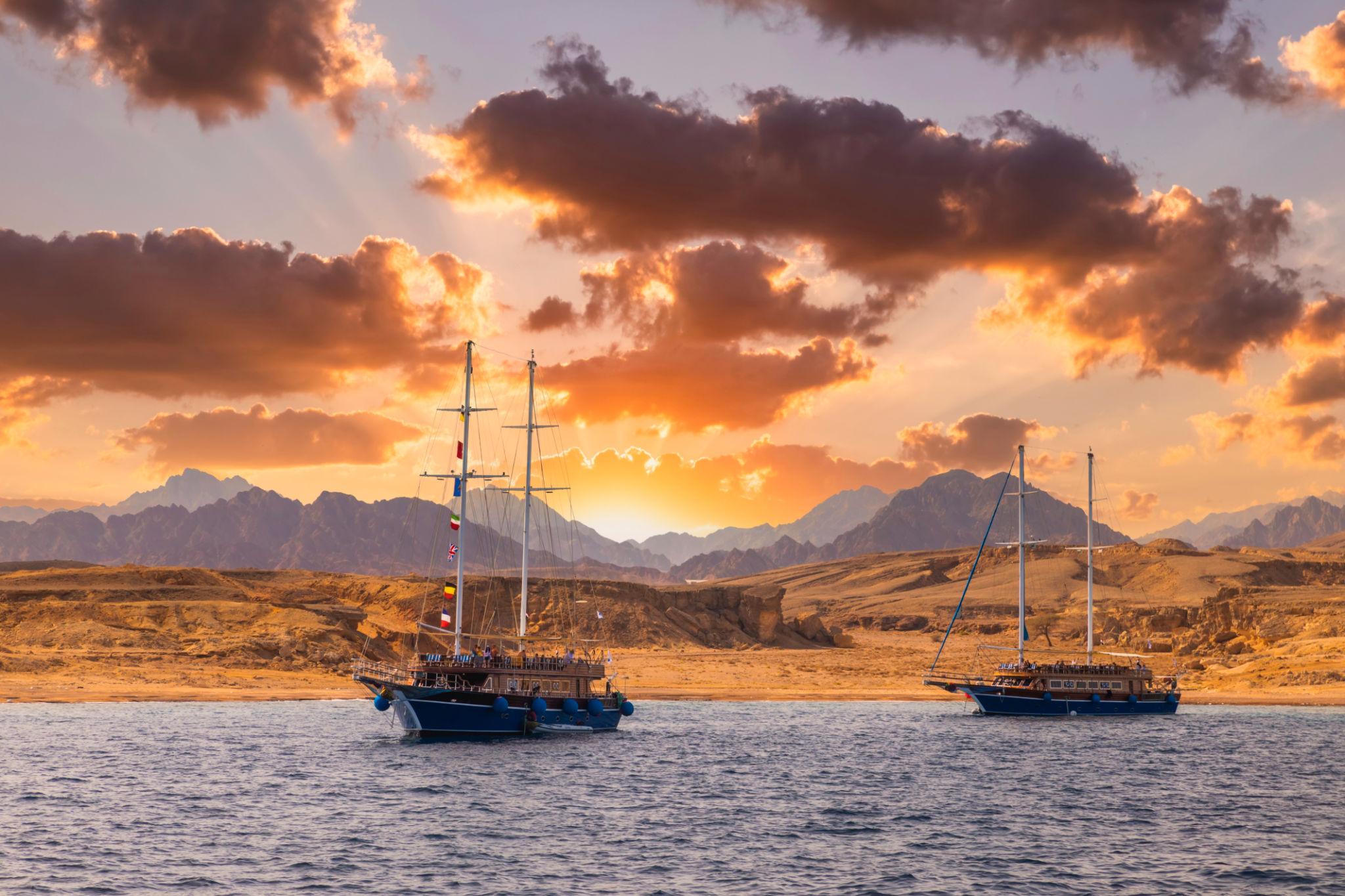 Two wooden sailing boats anchored on the Red Sea with desert mountains glowing at sunset