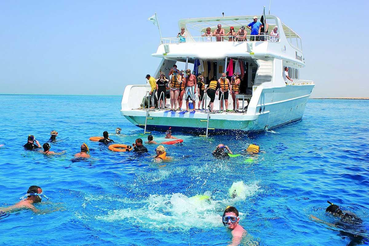 Tourists snorkeling in clear blue Red Sea waters beside a white double-deck excursion boat