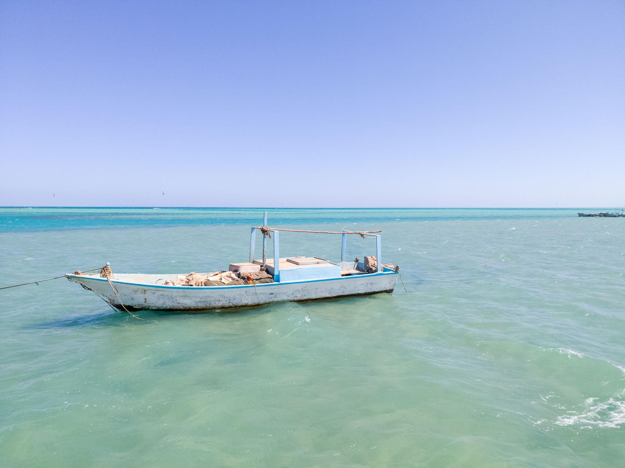 A weathered white and blue fishing boat anchored on calm turquoise Red Sea waters