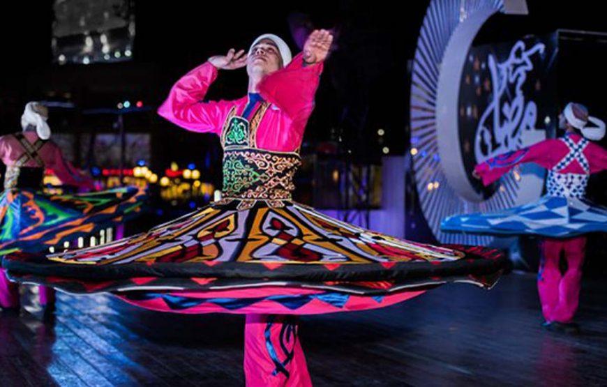 A performer in vibrant pink costume spins a colorful patterned skirt during a whirling dervish show