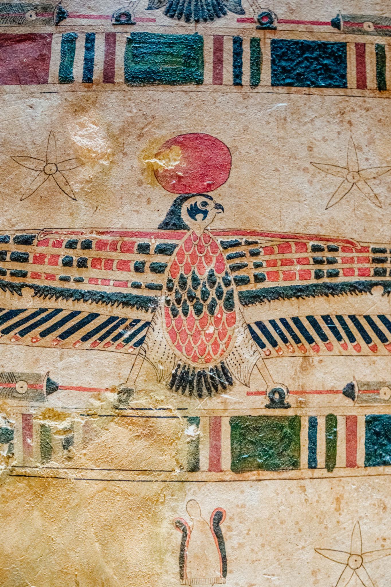 Colorful ancient Egyptian falcon deity with spread wings painted on a sarcophagus surface