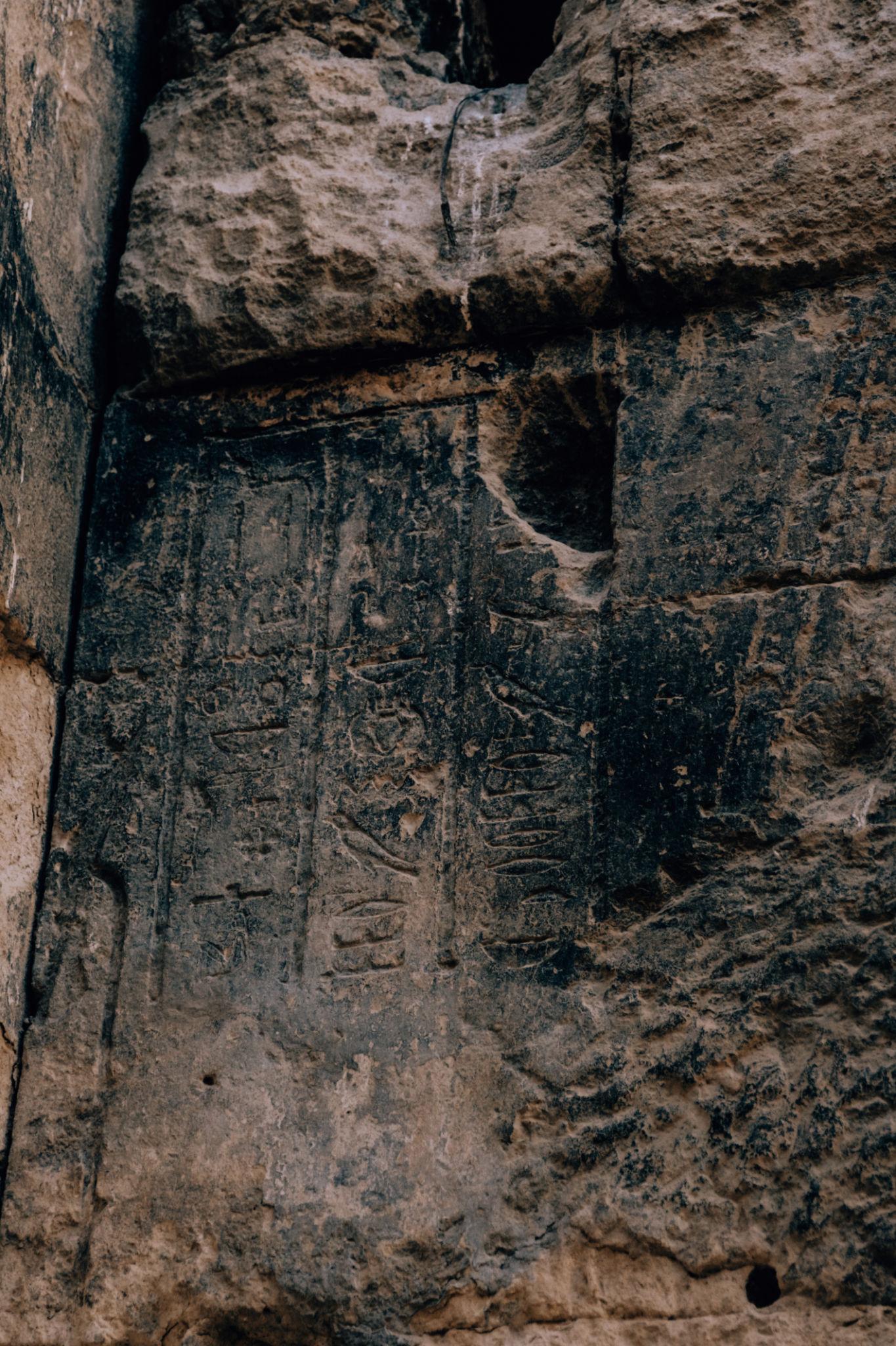 Weathered Egyptian hieroglyphs carved into a dark stone wall at Siwa Oasis