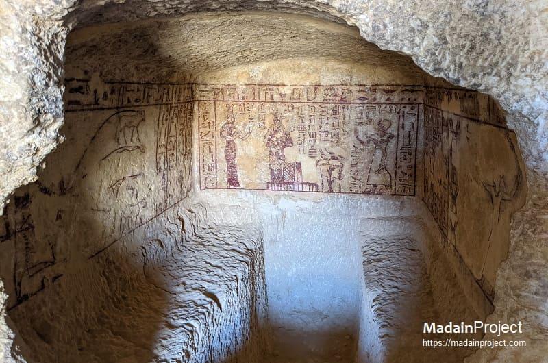 Interior of an ancient Egyptian rock-cut tomb with painted hieroglyphic murals on the back wall.