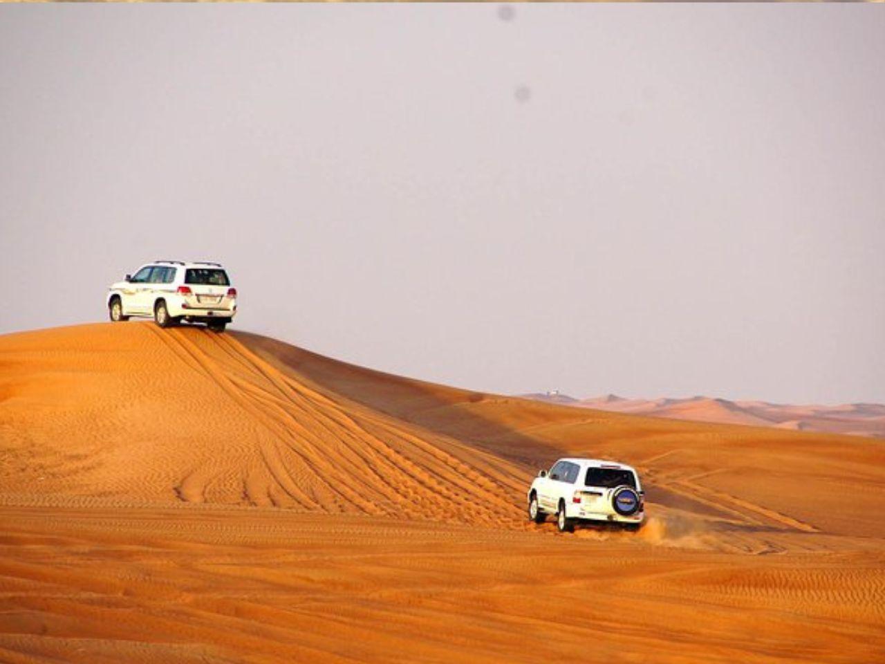 Two white 4x4 SUVs navigating steep orange sand dunes in the Siwa desert
