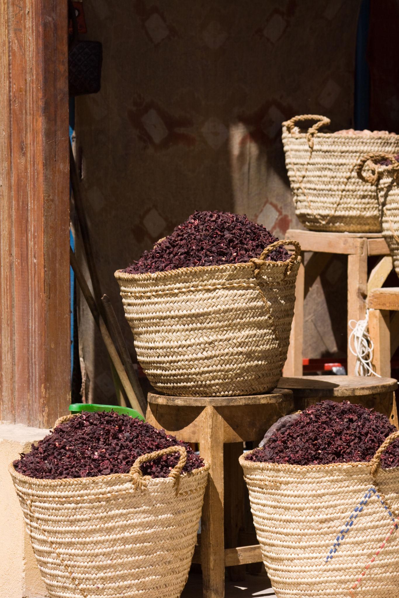 Large woven straw baskets overflowing with dried hibiscus flowers at a Siwa market stall
