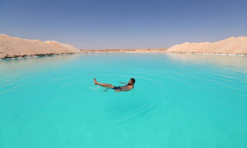 A man floats effortlessly on the vivid turquoise waters of a Siwa salt lake in the desert