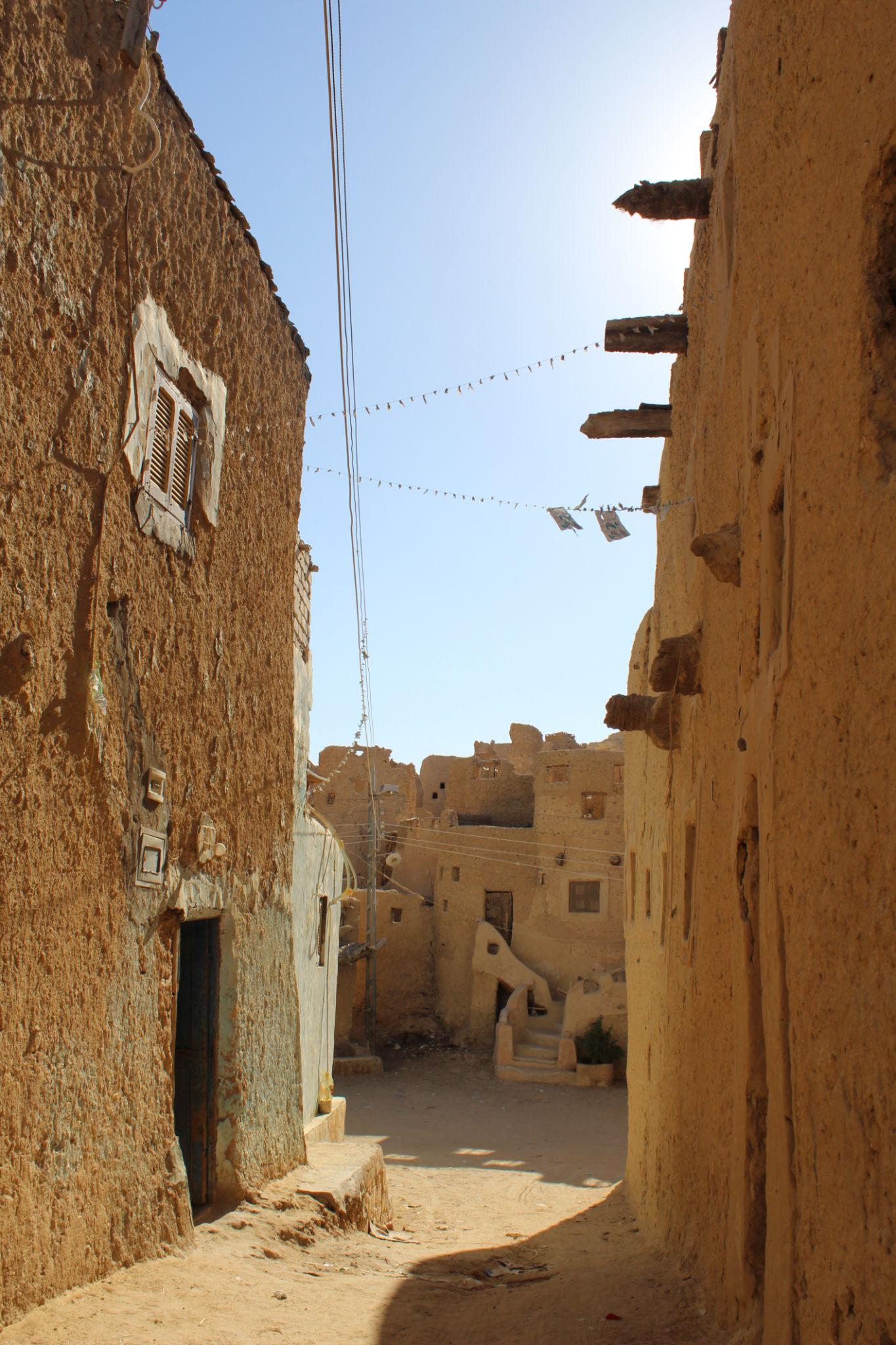 Narrow sandy alley between crumbling mud-brick buildings in Siwa's ancient old town