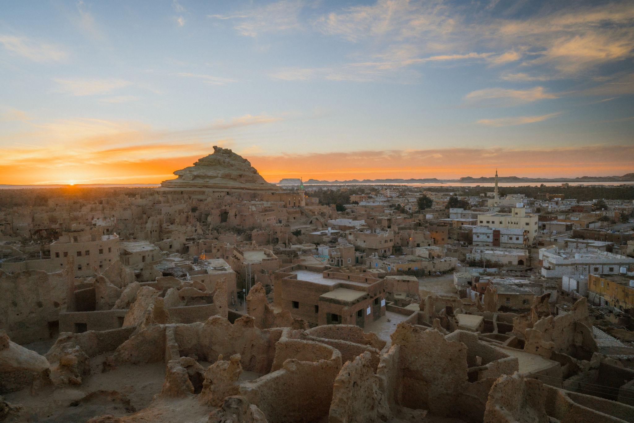 Aerial view of Siwa's mud-brick ruins and town at sunset with a rocky outcrop in the background