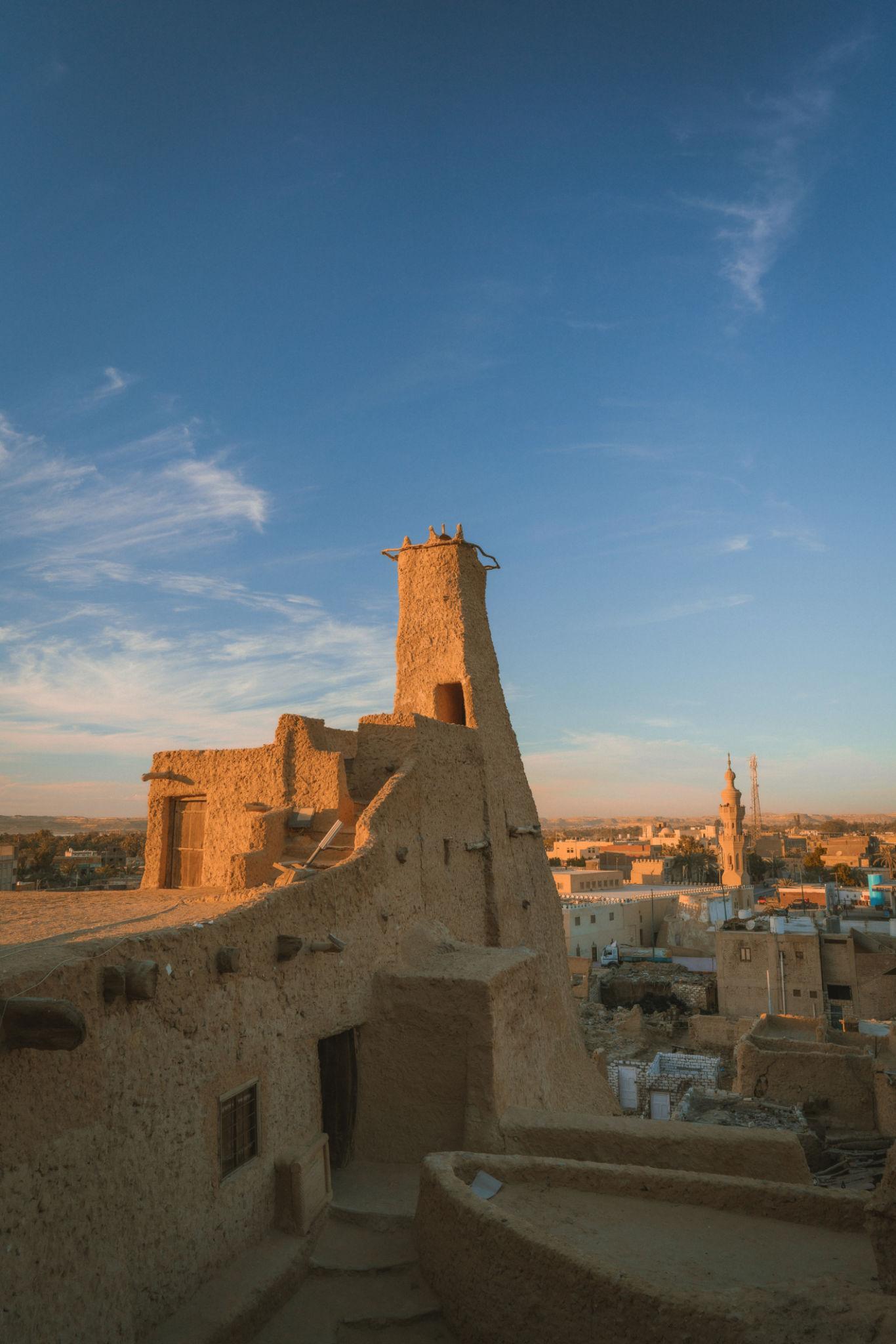 Ancient mud-brick Shali fortress tower glowing at sunset above Siwa Oasis town