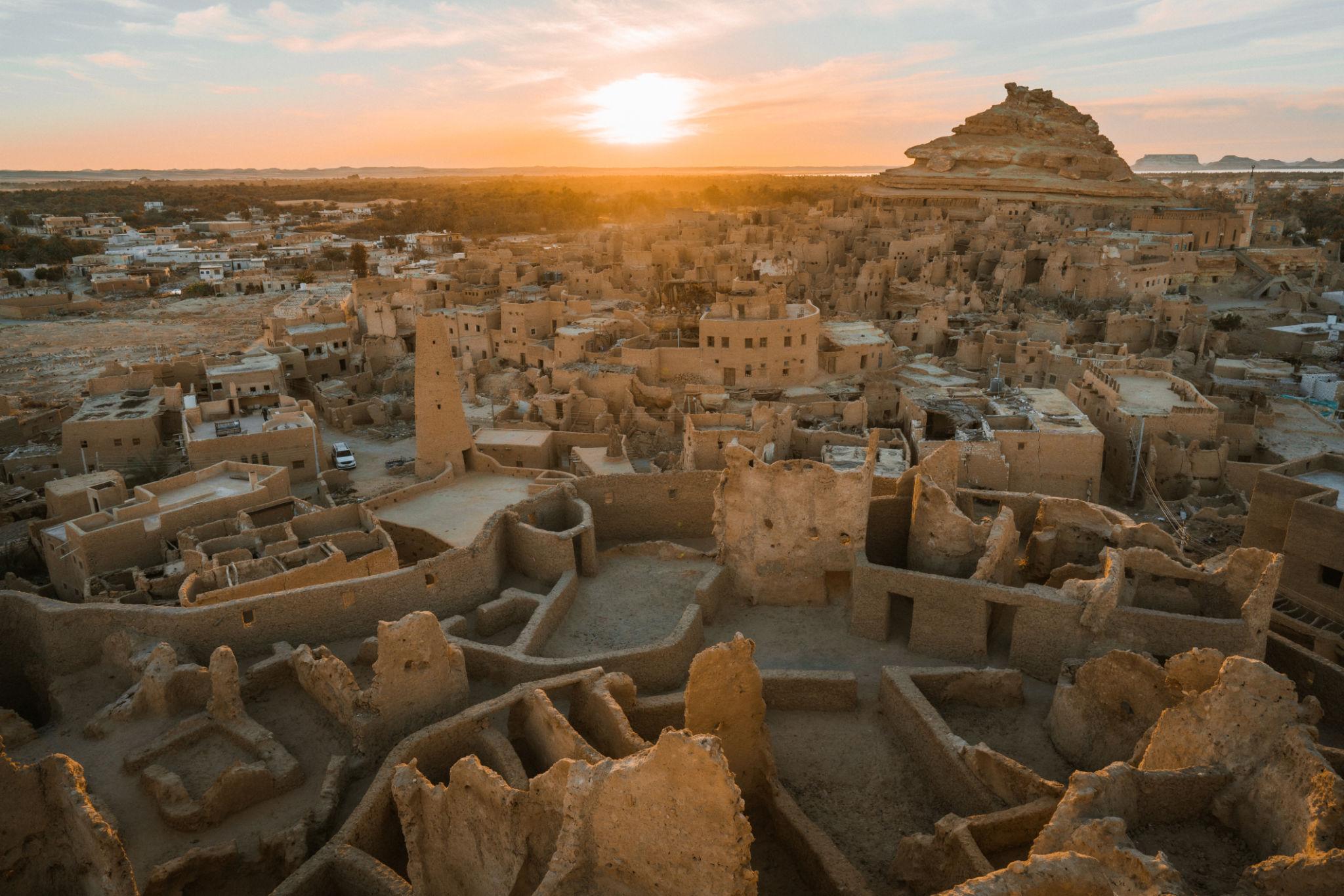Aerial view of Siwa's ancient mud-brick Shali fortress ruins glowing under a golden sunset