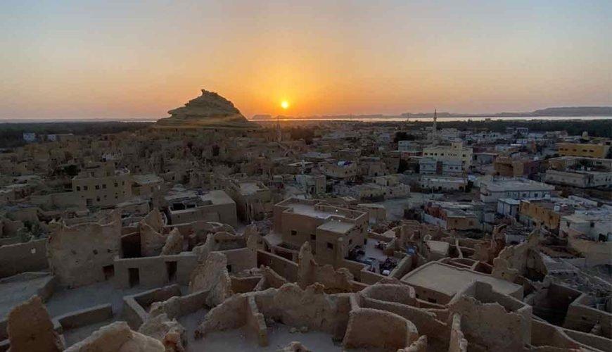 Aerial view of Siwa Oasis mud-brick ruins and town at sunset with rocky outcrop silhouetted