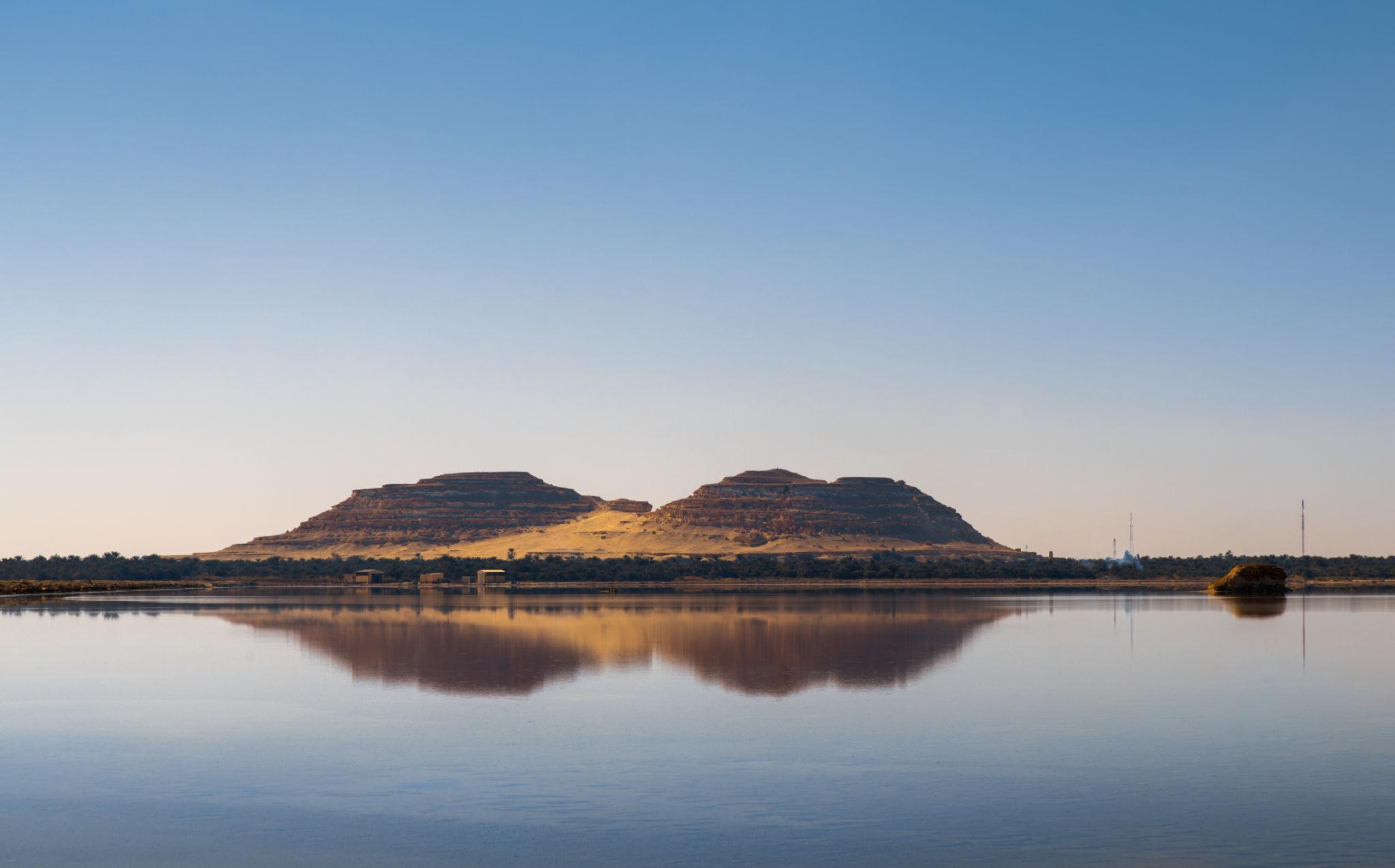 Two flat-topped sandstone buttes reflected in the still waters of a Siwa Oasis lake at dusk