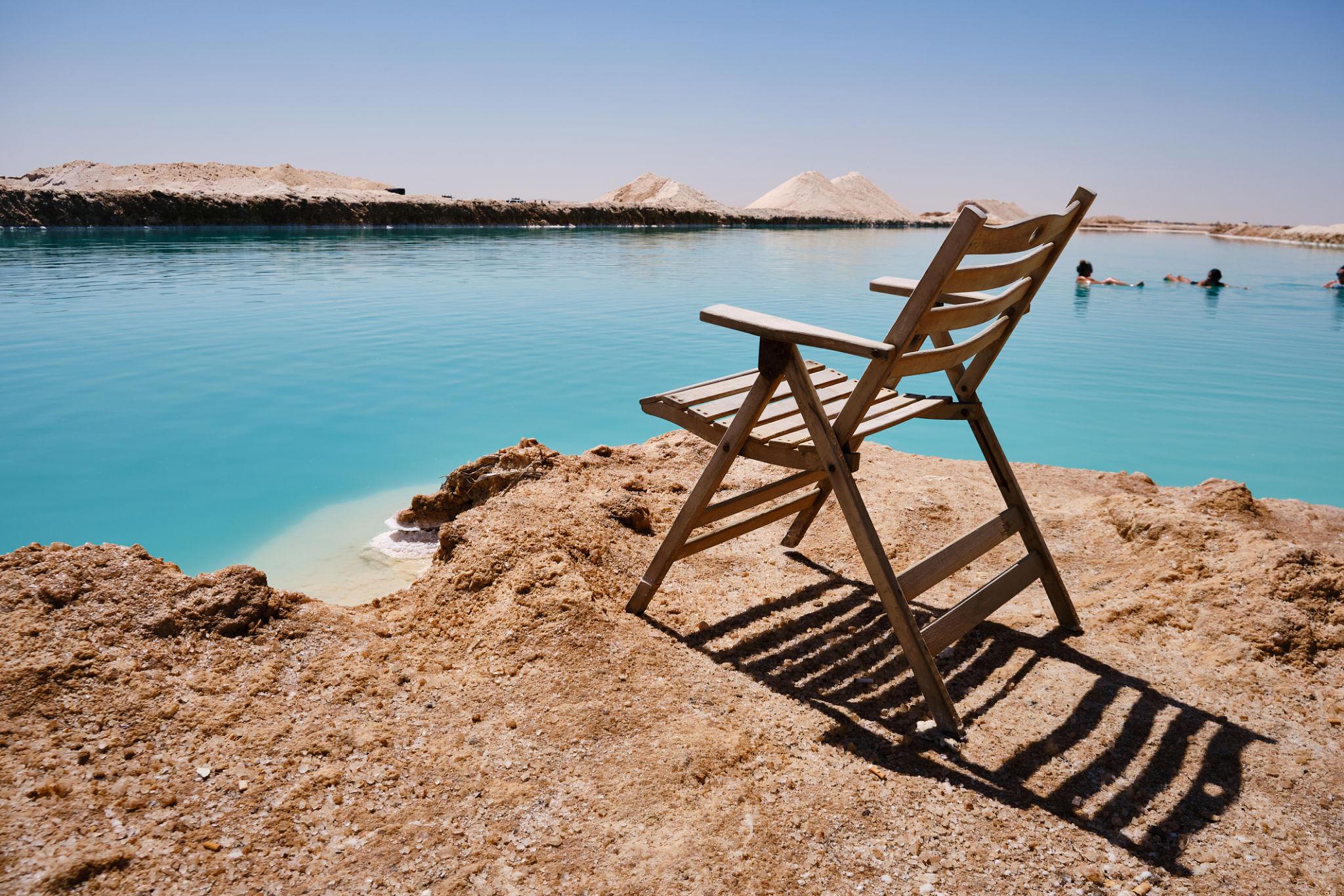 A wooden folding chair overlooking Siwa's turquoise salt lake under a clear desert sky