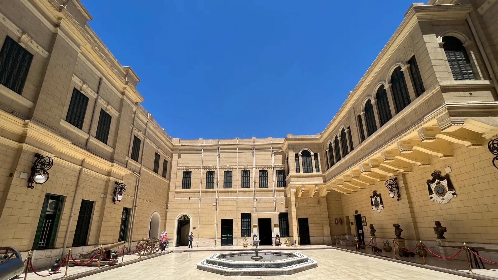 Sunlit sandstone courtyard of NMEC with central fountain, arched galleries, and historic cannons