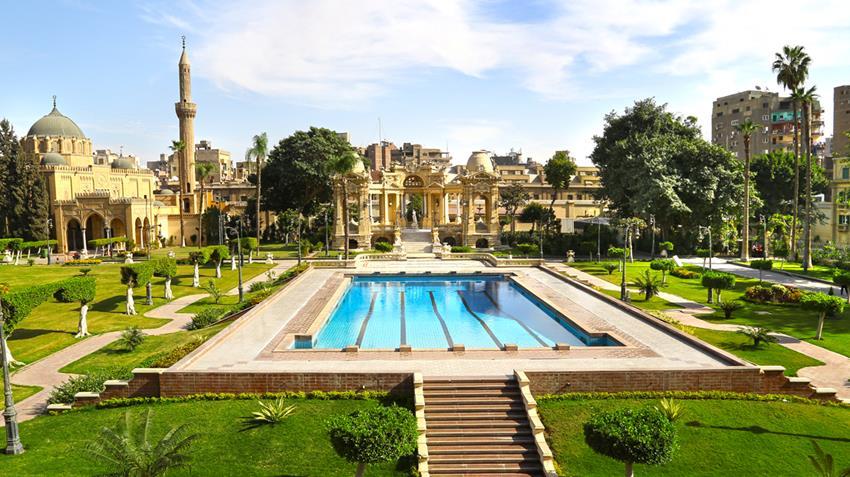 Ornate museum gardens with a rectangular pool, green lawns, and a mosque minaret beyond.