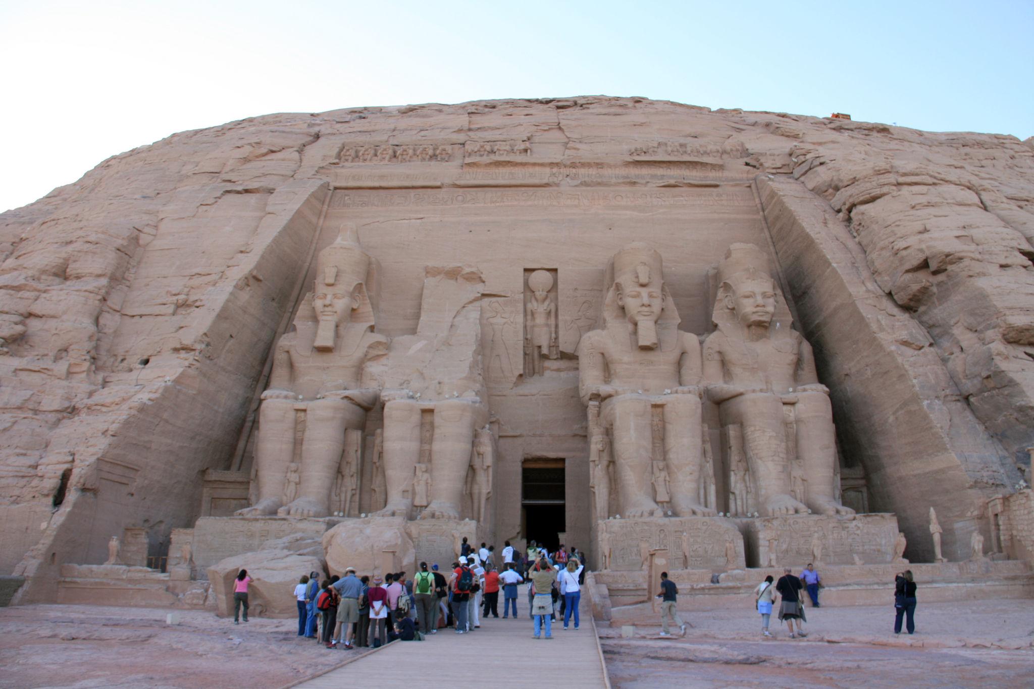 Tourists gather before the four giant seated statues of Ramesses II at Abu Simbel temple facade.