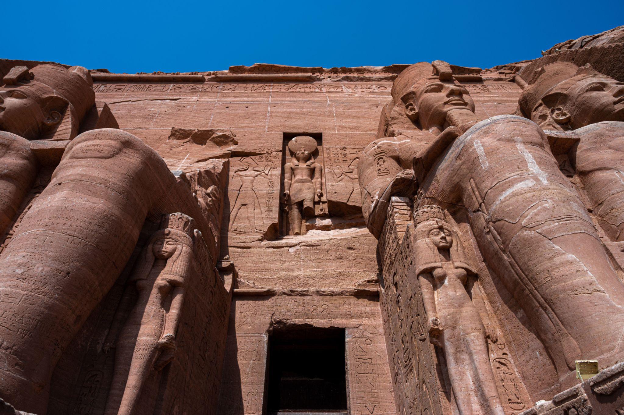 Upward view of Abu Simbel's massive rock-cut colossi and hieroglyph-covered facade under blue sky