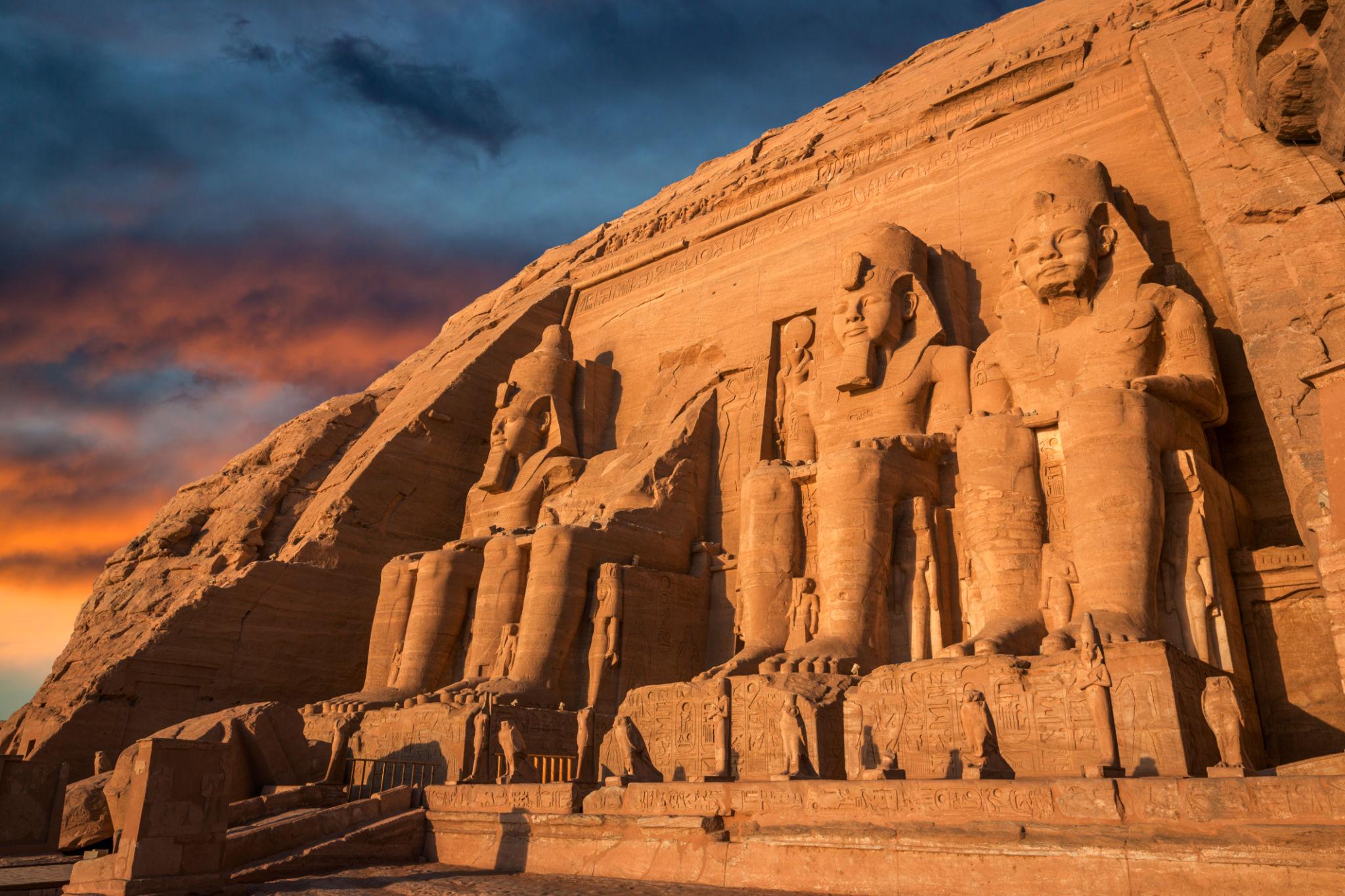 Four giant Ramesses II colossi carved into the sandstone facade of Abu Simbel at sunset
