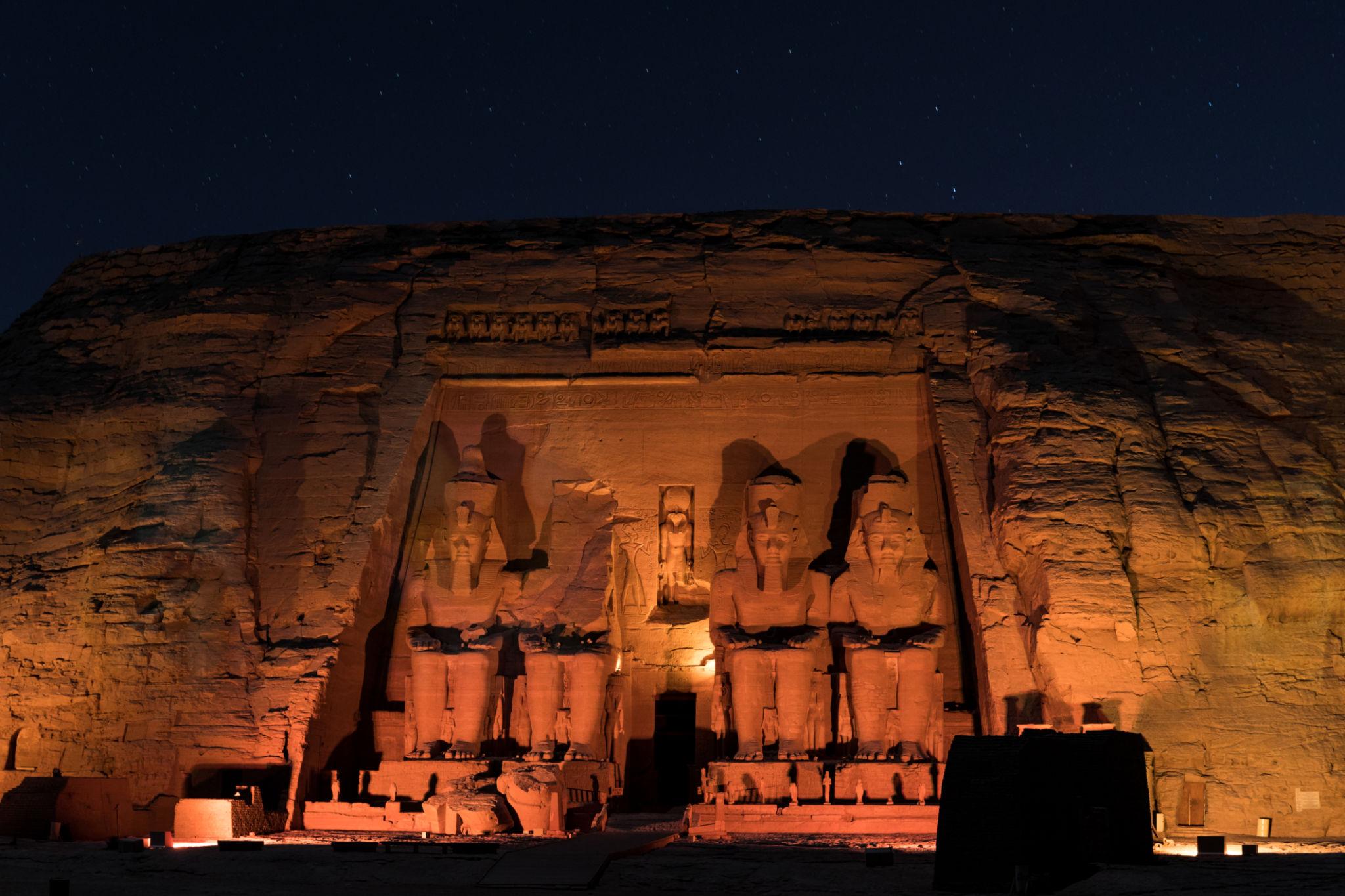 Four colossal statues of Ramesses II at Abu Simbel glowing under warm lights at night