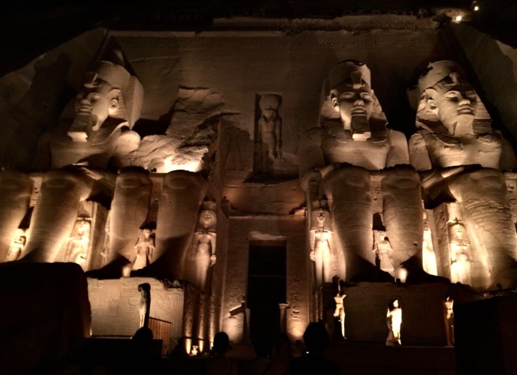 Four colossal statues of Ramesses II lit up dramatically against the dark night sky