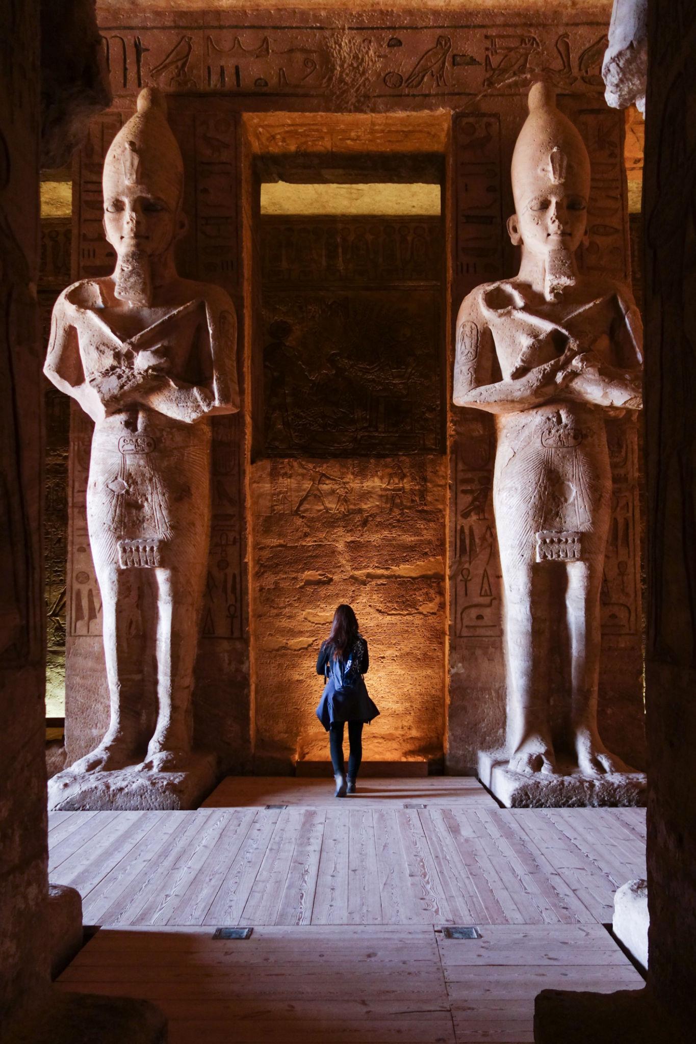 A lone visitor stands between two colossal Osiride statues inside Abu Simbel temple