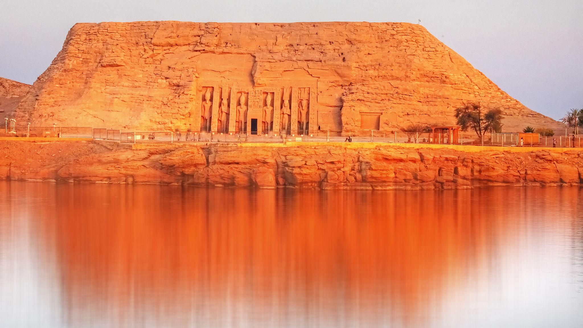 Small Temple of Nefertari at Abu Simbel reflected in the calm waters of Lake Nasser at golden hour
