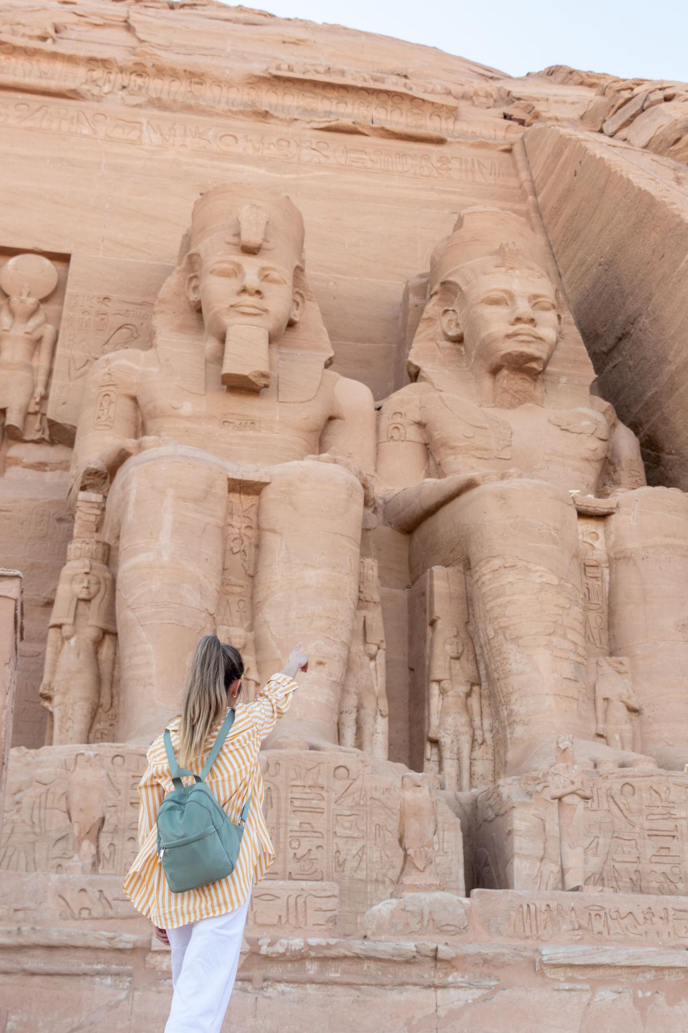 A woman in a striped shirt pointing up at the giant colossi statues at Abu Simbel temple