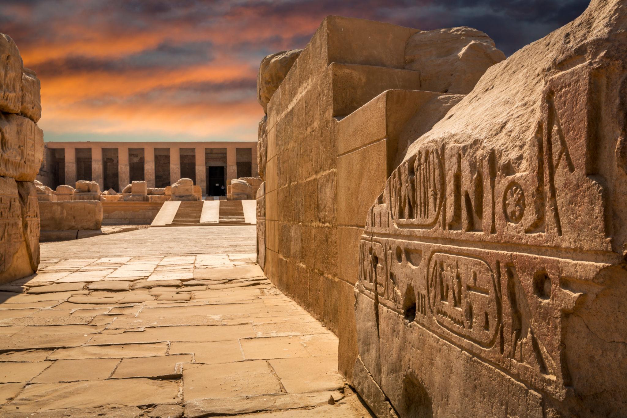 Temple of Seti I courtyard at sunset with carved reliefs in the foreground.