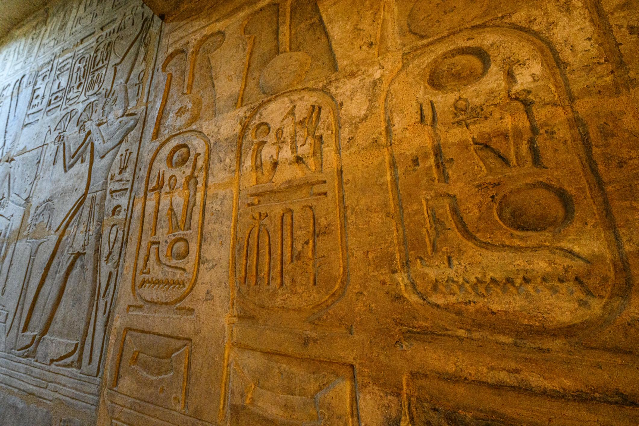 Sunlit cartouche reliefs glowing on an interior wall at Abydos Temple.